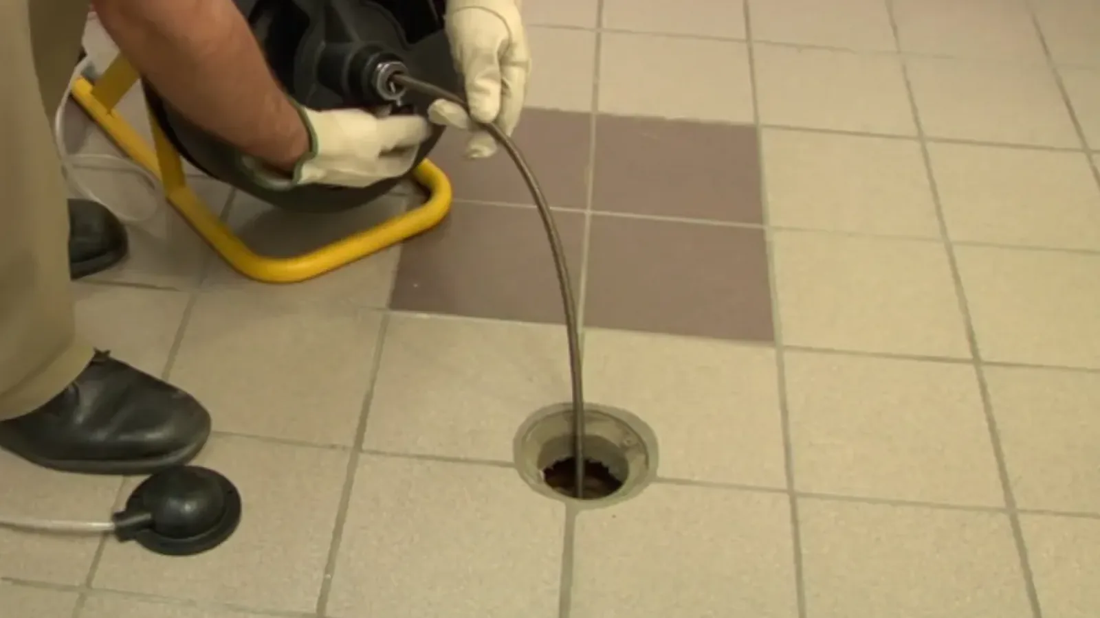 Plumber feeding a drain cable into a floor drain on a tiled floor